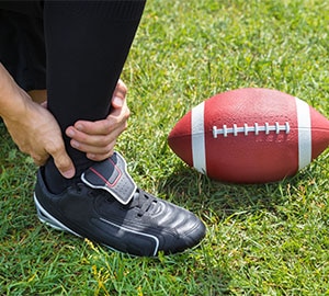 Sportif se tenant la cheville après une torsion, sur un terrain de football
